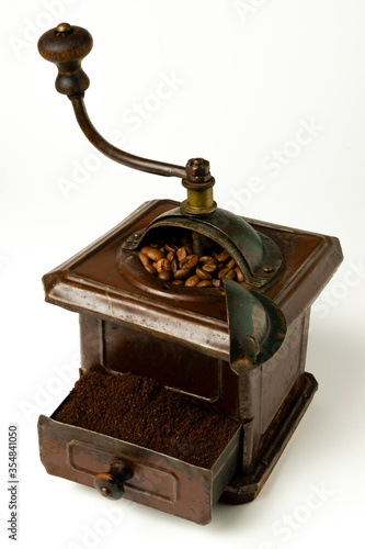 Molinillo de café marrón con granos de café en el interior y café molido en cajón sobre fondo blanco