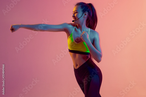 Photography Cute girl fitness instructor teaches Boxing or body combat online training remotely on a bright neon background