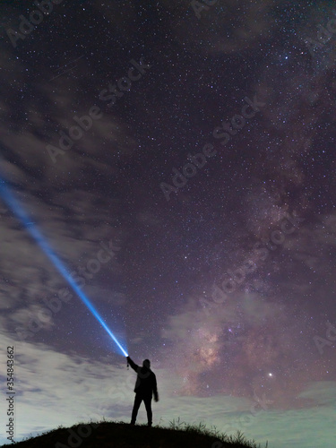 Silhouette of a man with a flashlight, observing beautiful, wide blue night sky with stars and Milky way galaxy. Astronomy, orientation, clear sky concept and background.