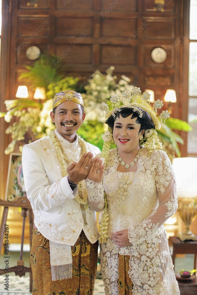 Smiling Javanese groom and bride showing they rings after masang cincin ceremony , with old wood for background.