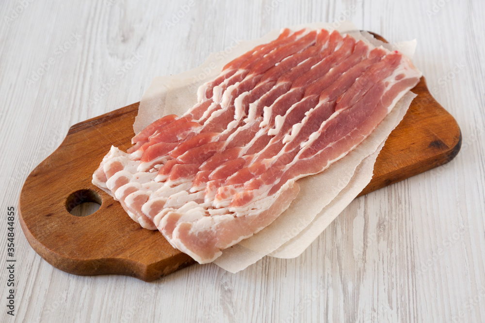 Uncooked Raw Bacon on a rustic wooden board on a white wooden table, side view. Uncooked Raw Bacon on a rustic wooden board on a white wooden table, side view.