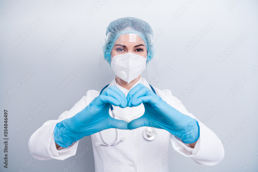 Photo of beautiful lady doc hospital making arms fingers heart figure good mood cardiac safety concept wear gloves mask coat facial plastic shield surgical cap isolated grey color background Photo of beautiful lady doc hospital making arms fingers heart figure good mood cardiac safety concept wear gloves mask coat facial plastic shield surgical cap isolated grey color background