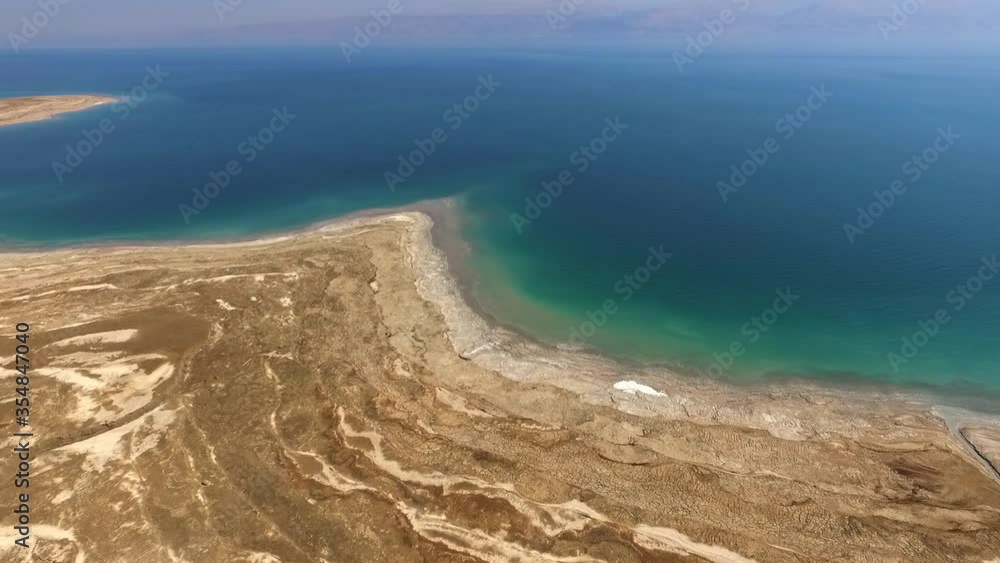 Aerial shot of rock formation by dead sea against mountains, drone flying forward over salt lake on sunny day Aerial shot of rock formation by dead sea against mountains, drone flying forward over salt lake on sunny day