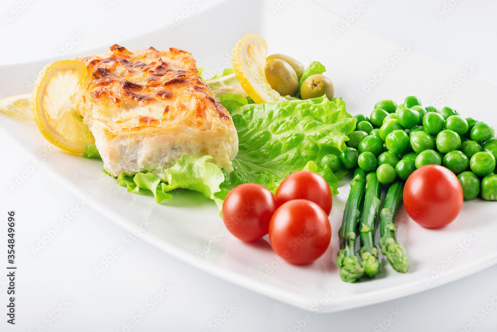 Cod fillet baked with cheese and onions with a garnish from an asparagus and green peas. On white background. High key. Selective focus.