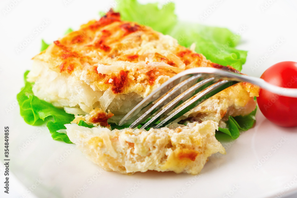 Cod fillet baked with cheese and onions with a garnish from an asparagus and green peas. On white background. High key. Selective focus. Close up. Cod fillet baked with cheese and onions with a garnish from an asparagus and green peas. On white background. High key. Selective focus. Close up.