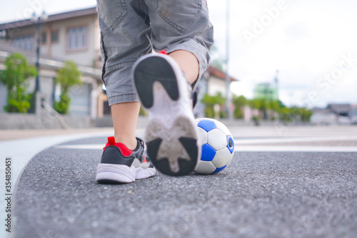 Low angle view of kid legs running and kicking soccer ball on cement ground