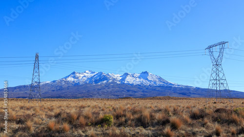 Snow on Mount Ruapehu, New Zealand. In the foreground, power pylons run through the tussock of the Rangipo Desert