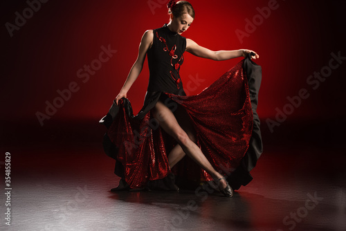 young and beautiful woman touching dress while dancing flamenco on red