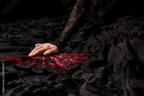 cropped view of young flamenco dancer in dress holding fan isolated on black