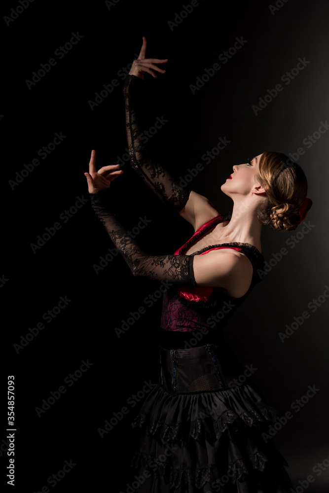 young and elegant woman gesturing while dancing flamenco on black