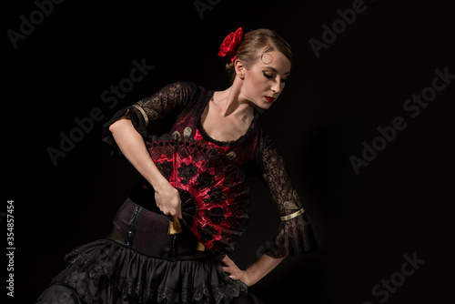 elegant flamenco dancer with hand on hip holding fan and dancing isolated on black