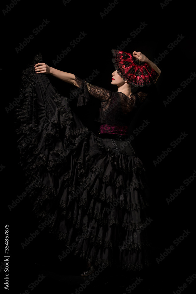 young and beautiful dancer holding fan while dancing flamenco isolated on black