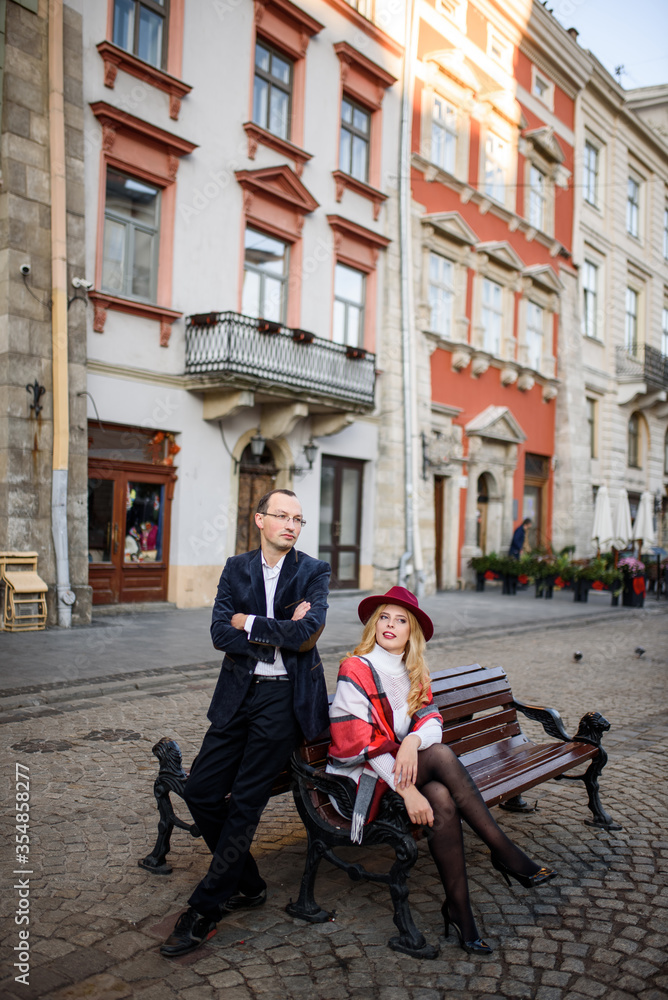Obraz premium Adult married couple sits on a bench against the background of the old city.