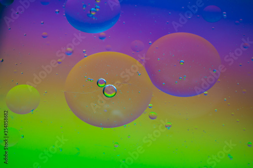 Fototapeta Naklejka Na Ścianę i Meble -  Bubbles of vegetable oil in clear water on a glass and transparent lid from a frying pan on colored paper.