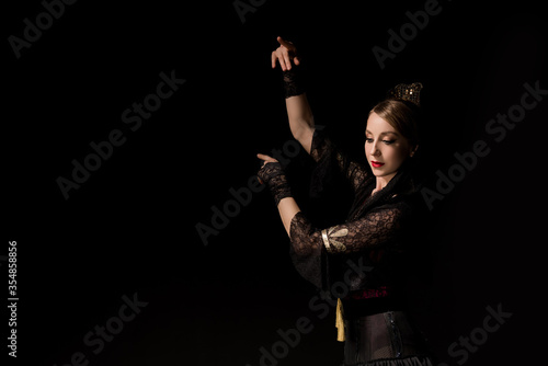 elegant flamenco dancer dancing and gesturing while looking down isolated on black