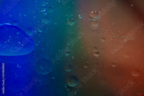 Bubbles of vegetable oil in clear water on a glass and transparent lid from a frying pan on colored paper.