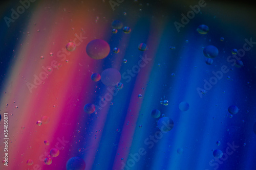 Bubbles of vegetable oil in clear water on a glass and transparent lid from a frying pan on colored paper.