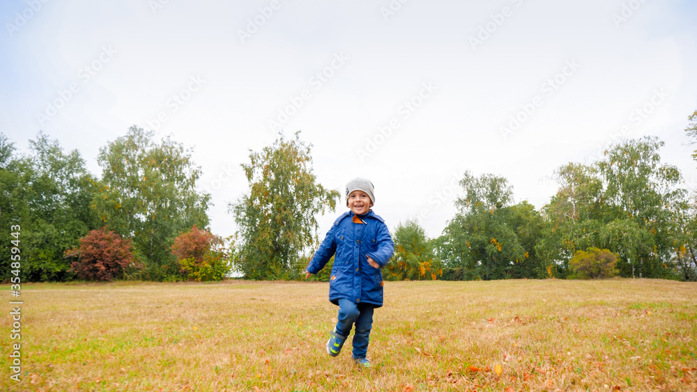 Happy smiling toddler boy in jacket running on field with dry grass on cloudy autumn day Happy smiling toddler boy in jacket running on field with dry grass on cloudy autumn day