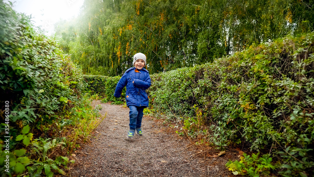 Obraz premium Happy laughing little boy in jacket running in bush labyrinth at autumn park