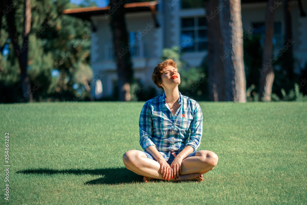 Beautiful young woman with short haircut enjoying nature and yoga meditation outdoors aon green lawn in sunny summer day. Healthy girl in green grass. Relax and recreation concept Beautiful young woman with short haircut enjoying nature and yoga meditation outdoors aon green lawn in sunny summer day. Healthy girl in green grass. Relax and recreation concept