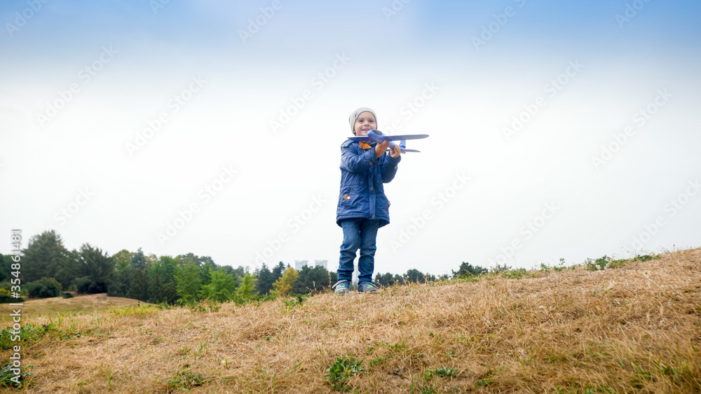 Happy smiling little boy holding and playing with toy airplane on field Happy smiling little boy holding and playing with toy airplane on field