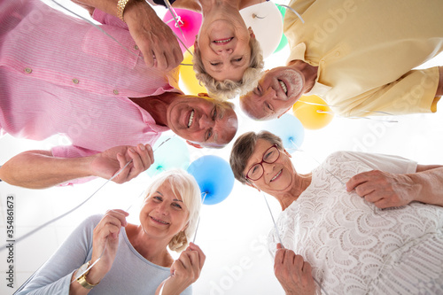 Bild auf Leinwand Low angle of happy senior friends in the circle with balloons during birthday pa