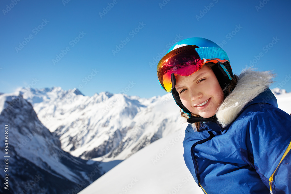 Happy portrait of a girl in ski helmet and open mask smile over mountain summit peaks