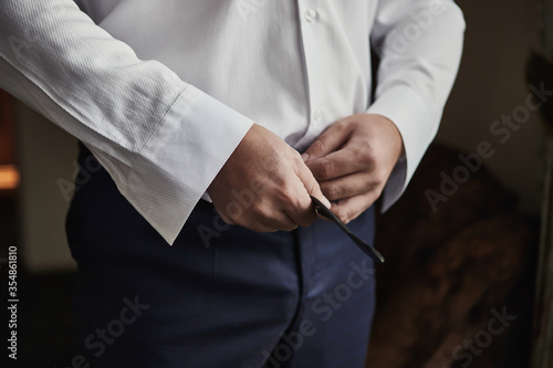Businessman putting on a belt  fashion and clothing concept groom getting ready in the morning before ceremony