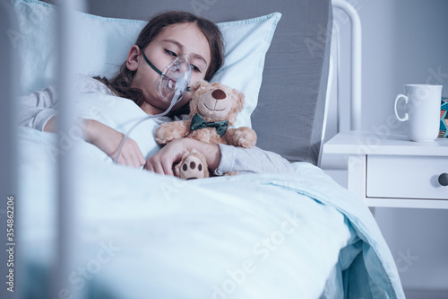 Konstfotografi Girl suffering from pneumonia lying in a hospital bed with oxygen mask and teddy