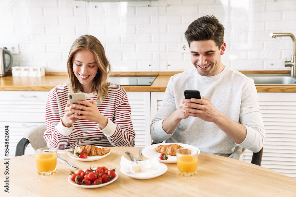 Portrait of smiling couple using smartphones while having breakfast