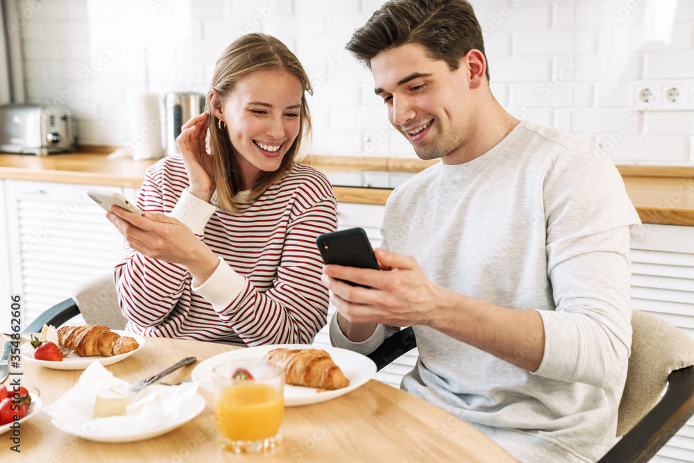 Portrait of couple using smartphones and talking while having breakfast Portrait of couple using smartphones and talking while having breakfast