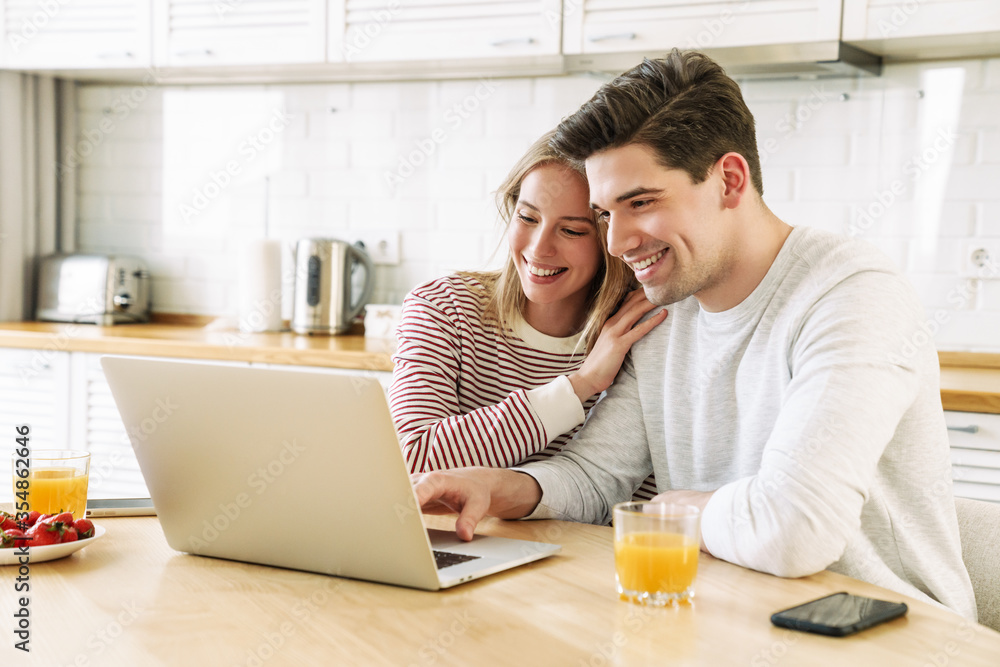 Portrait of couple using laptop and smiling while having breakfast Portrait of couple using laptop and smiling while having breakfast