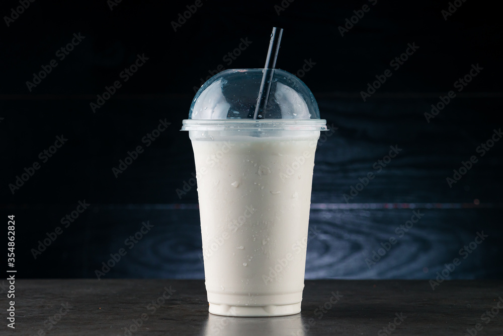 Vanilla Milkshake in Plastic Glass on a Dark Background. Vanilla