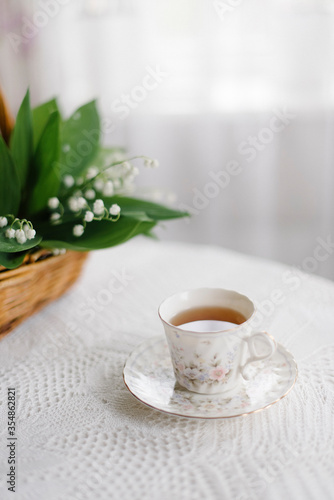 Fototapeta Naklejka Na Ścianę i Meble -  lilies of the valley in the basket and a cup of tea