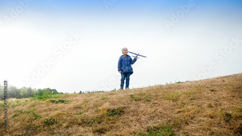 Smiling little boy standing on the field and holding toy airplane