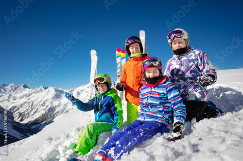 Fun group portrait of kids sit together in snow over beautiful mountain range tops in Alps
