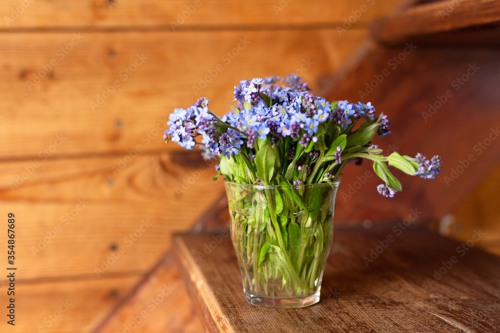 Blue wildflowers in a glass cup on a wooden background. Forget me nots. Blue wildflowers in a glass cup on a wooden background. Forget me nots.