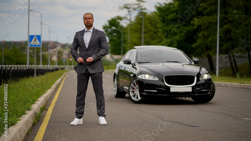 Elegant man in a suit without tie next to a car on the highway