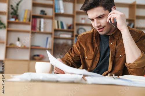 Image of handsome man talking cellphone while working with documents