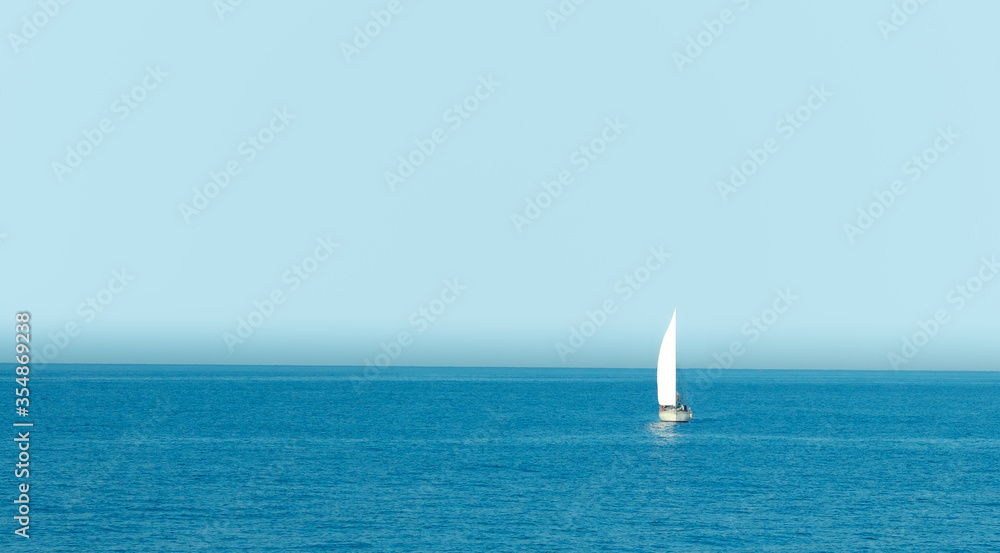 Boat with sail sailing in Spain sea with clear sky at sunrise
