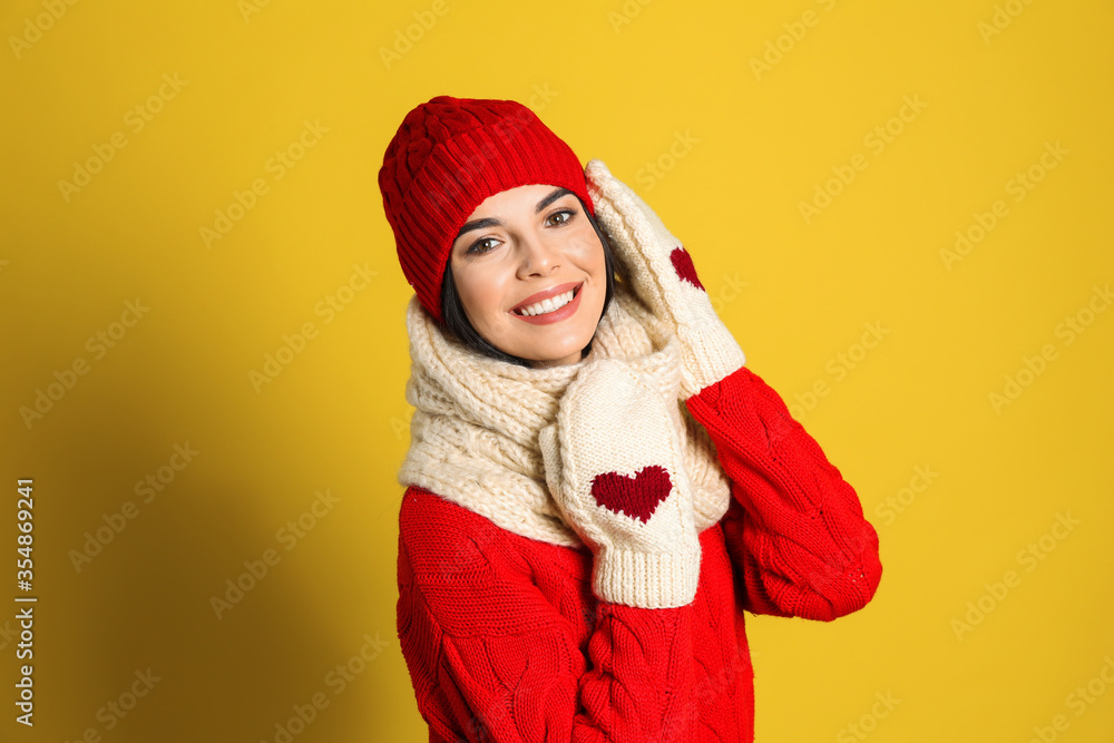 Young woman wearing warm sweater, scarf, mittens and hat on yellow background. Winter season Young woman wearing warm sweater, scarf, mittens and hat on yellow background. Winter season