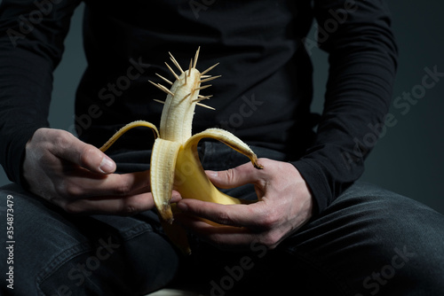 sexually transmitted diseases concept. A man in black with a prickly banana in his hand, on a gray background. Muditsin concept of sexually transmitted diseases.