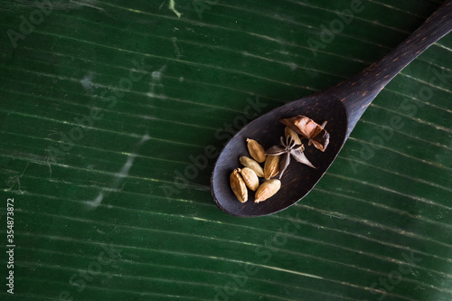 Cooking spices on banana leaf. Cardamom and star anise on a wooden spatula. Buah pelaga, bunga lawang, photo