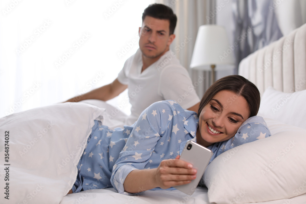 Fototapeta premium Distrustful man peering into girlfriend's smartphone at home. Jealousy in relationship