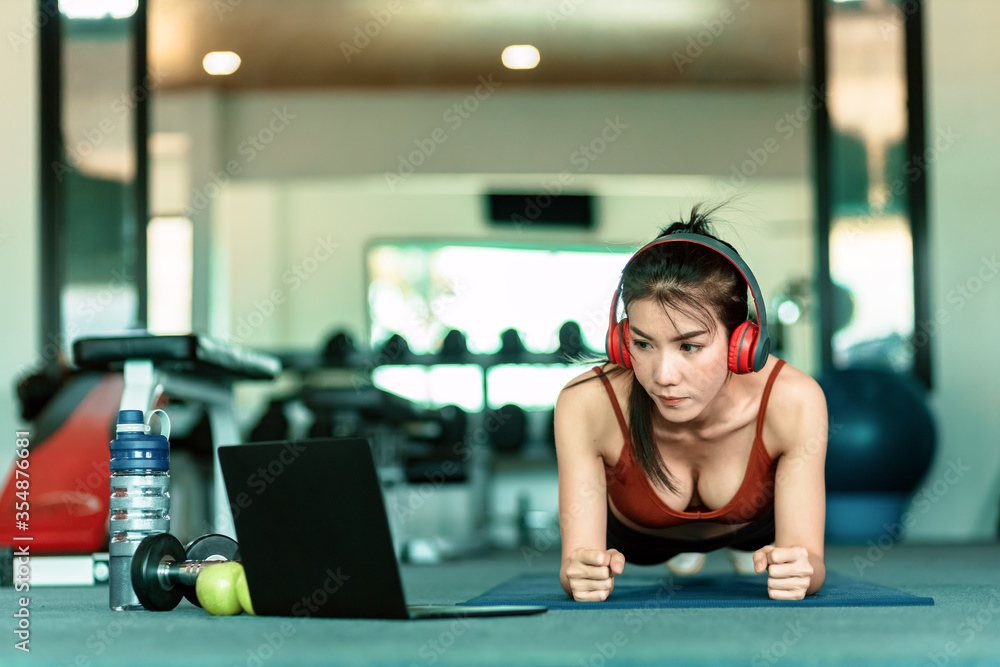 Full-length of young beautiful woman in sportswear doing plank at gym. Women and ear phone listen music between workout. Full-length of young beautiful woman in sportswear doing plank at gym. Women and ear phone listen music between workout.