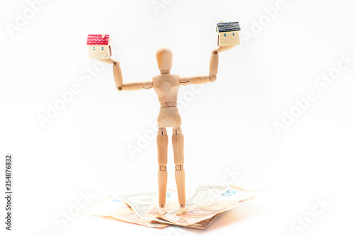 Wooden doll holding two miniature houses on some euro and dollar bills