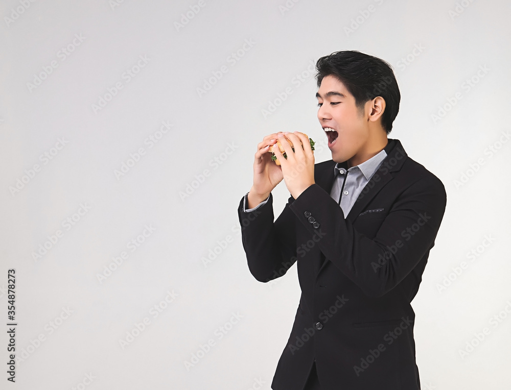 Asian young and handsome business man wearing dark suit standing on white background , open his mouth to eat hamburger . Asian young and handsome business man wearing dark suit standing on white background , open his mouth to eat hamburger .