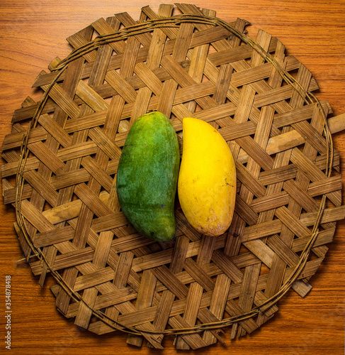 A green and yellow mangoes are placed on a bamboo weave.