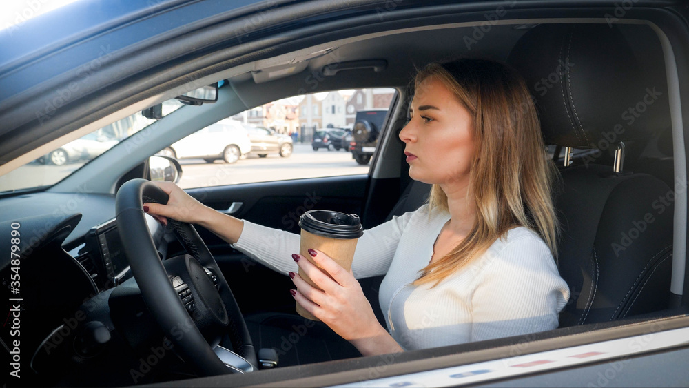 Portrait of beautiful blonde woman driving a car and drinking coffe from paper cup