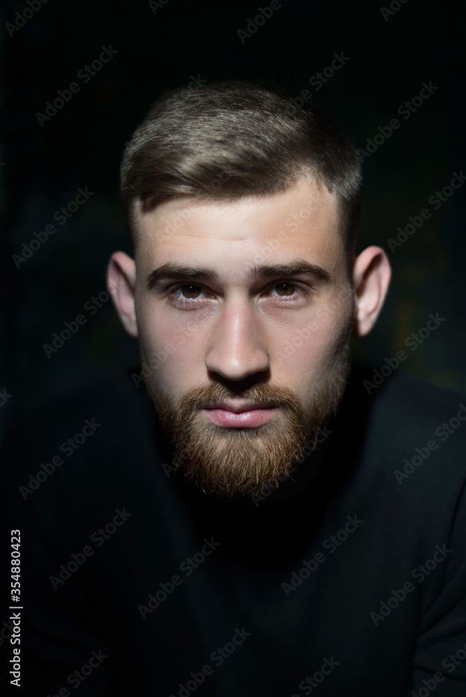portrait of a bearded eared young guy of twenty-five years old, in black clothes, on a dark background. Studio portrait on black portrait of a bearded eared young guy of twenty-five years old, in black clothes, on a dark background. Studio portrait on black